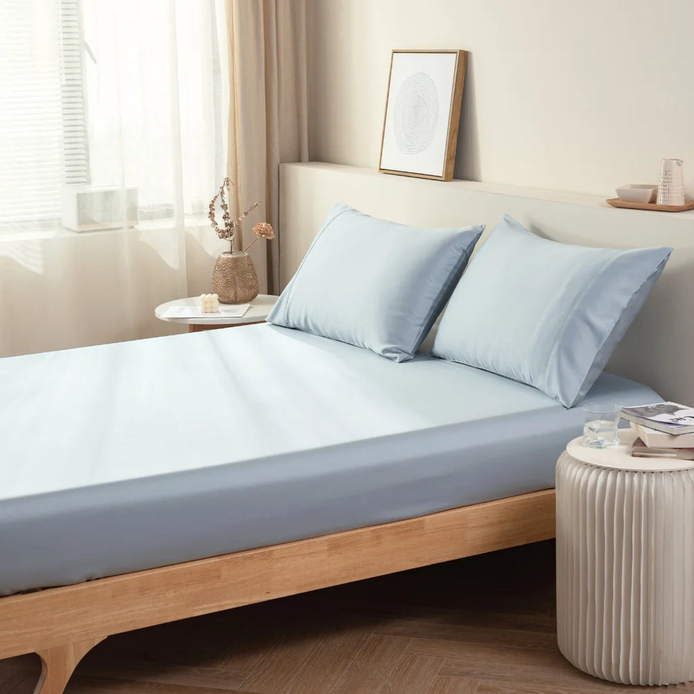 A neatly made bed with Linenly's light blue Bamboo Fitted Sheet in a serene and minimalistic bedroom setting.
