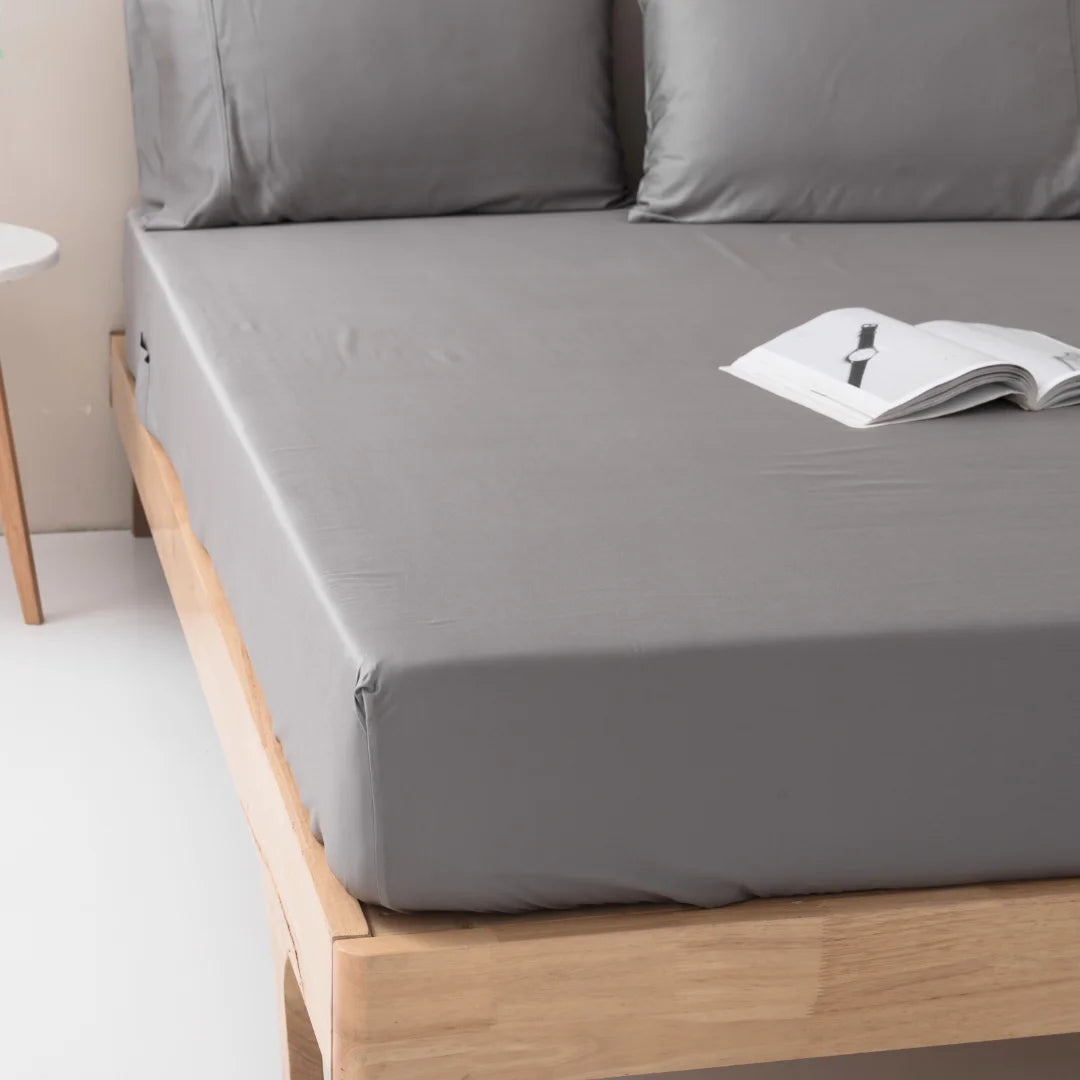 A neatly made bed with Linenly Stone Grey Bamboo Fitted Sheets, suggesting a cozy reading spot.