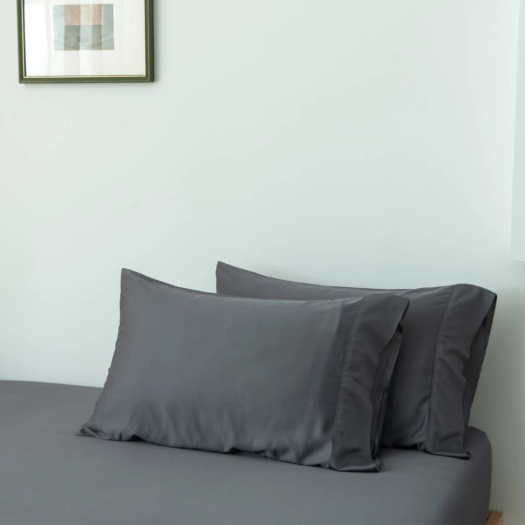 A minimalist bedroom with a neatly made bed covered with gray sheets, two matching pillows encased in Linenly's Granite Grey Bamboo Pillowcase Set, and a framed abstract painting on the wall above.