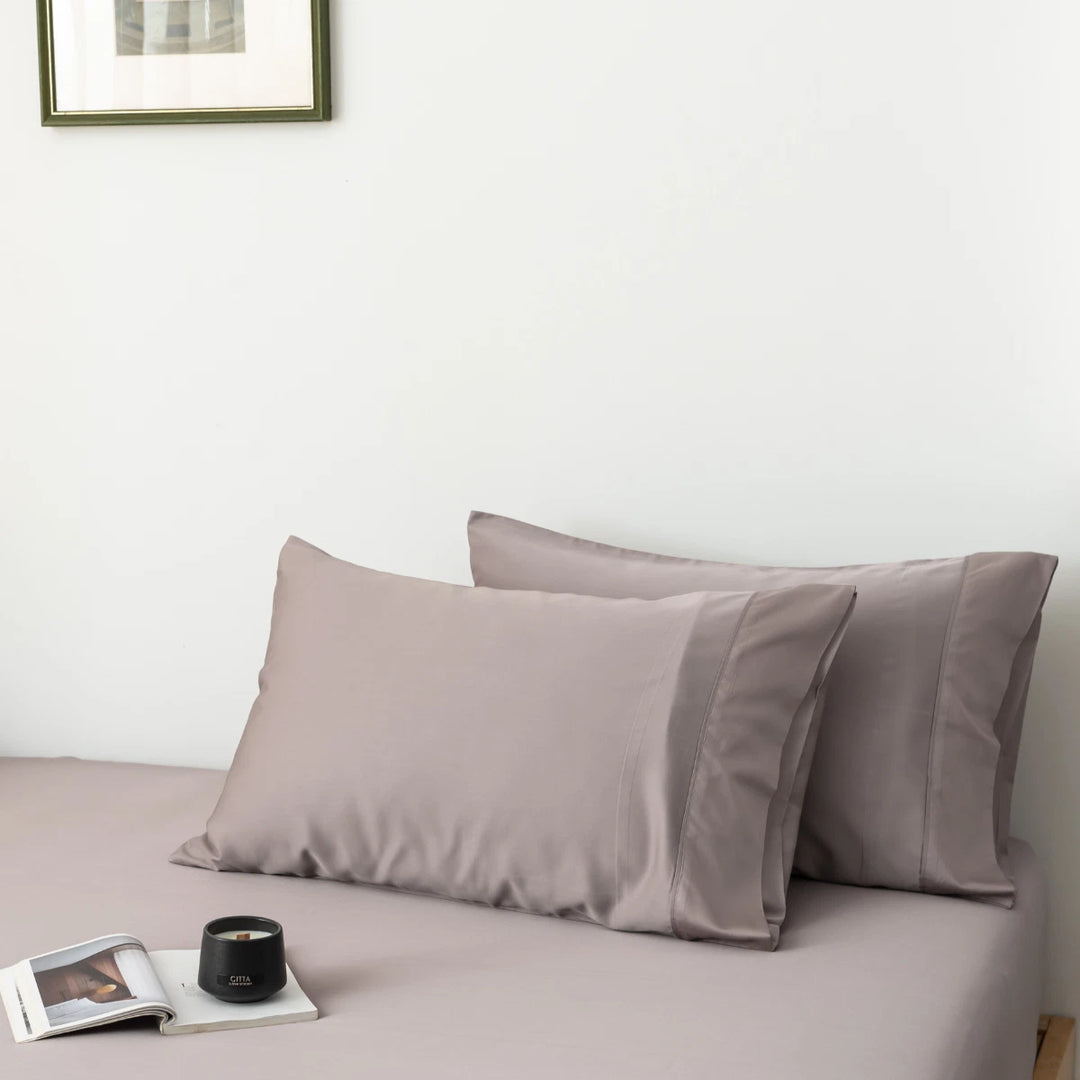 A neatly made bed with a pair of taupe pillows enveloped in Linenly's Bamboo Pillowcase Set - Stone Terrace, a magazine, and a cup of coffee on the side, creating a tranquil and cozy atmosphere in a room.