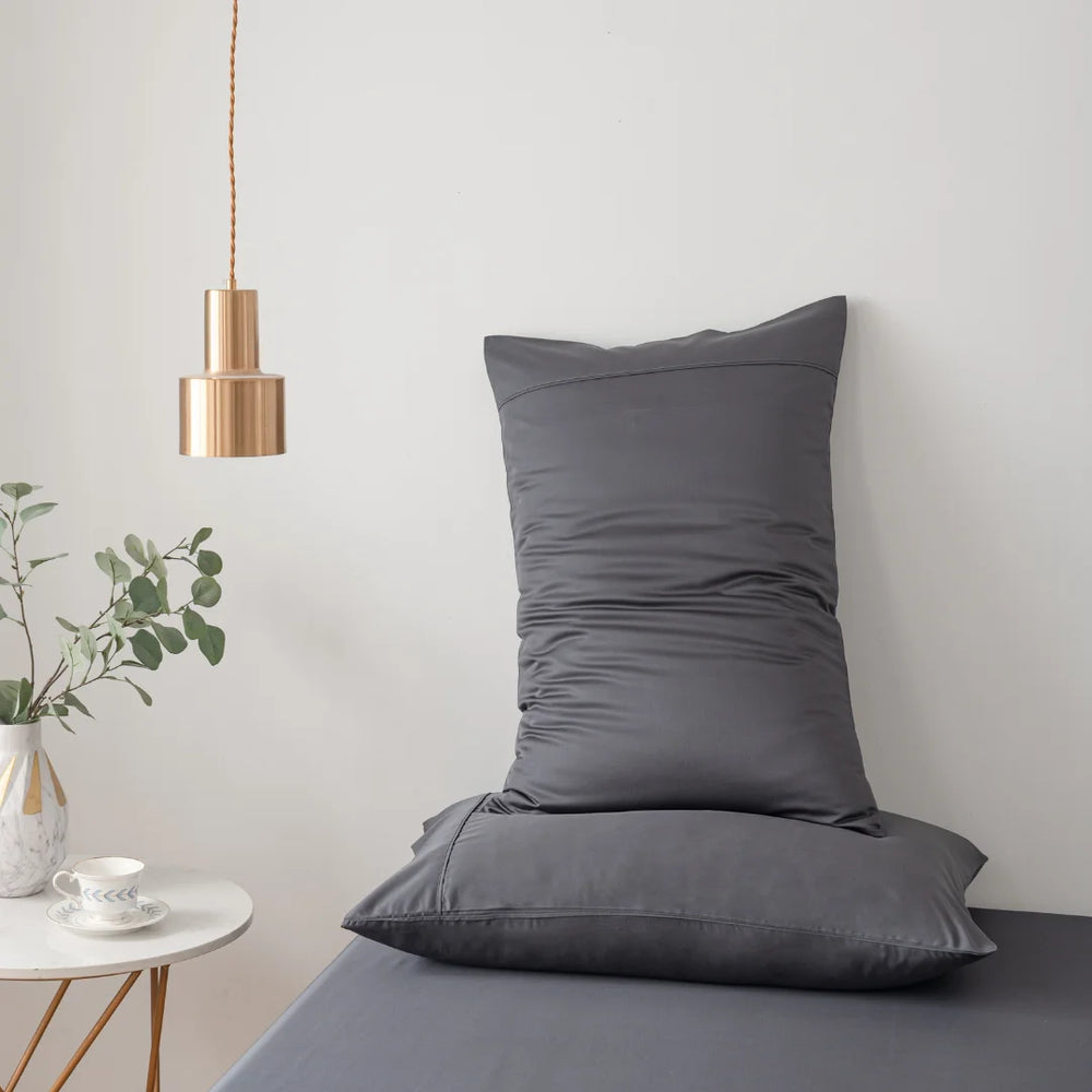 A minimalist interior featuring a gray cushion on a matching bench, with a gold pendant lamp above and a small plant with Linenly organic bamboo Charcoal pillowcases on the side, creating a serene and stylish corner.