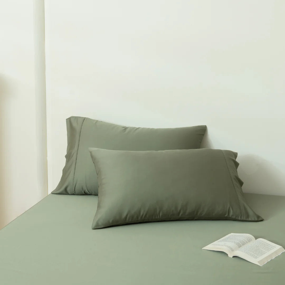A serene setting with Linenly's Bamboo Pillowcase Set in Moss on a neatly made bed complementing a matching sheet, with an open book invitingly placed on the bed, suggesting a quiet space for reading.