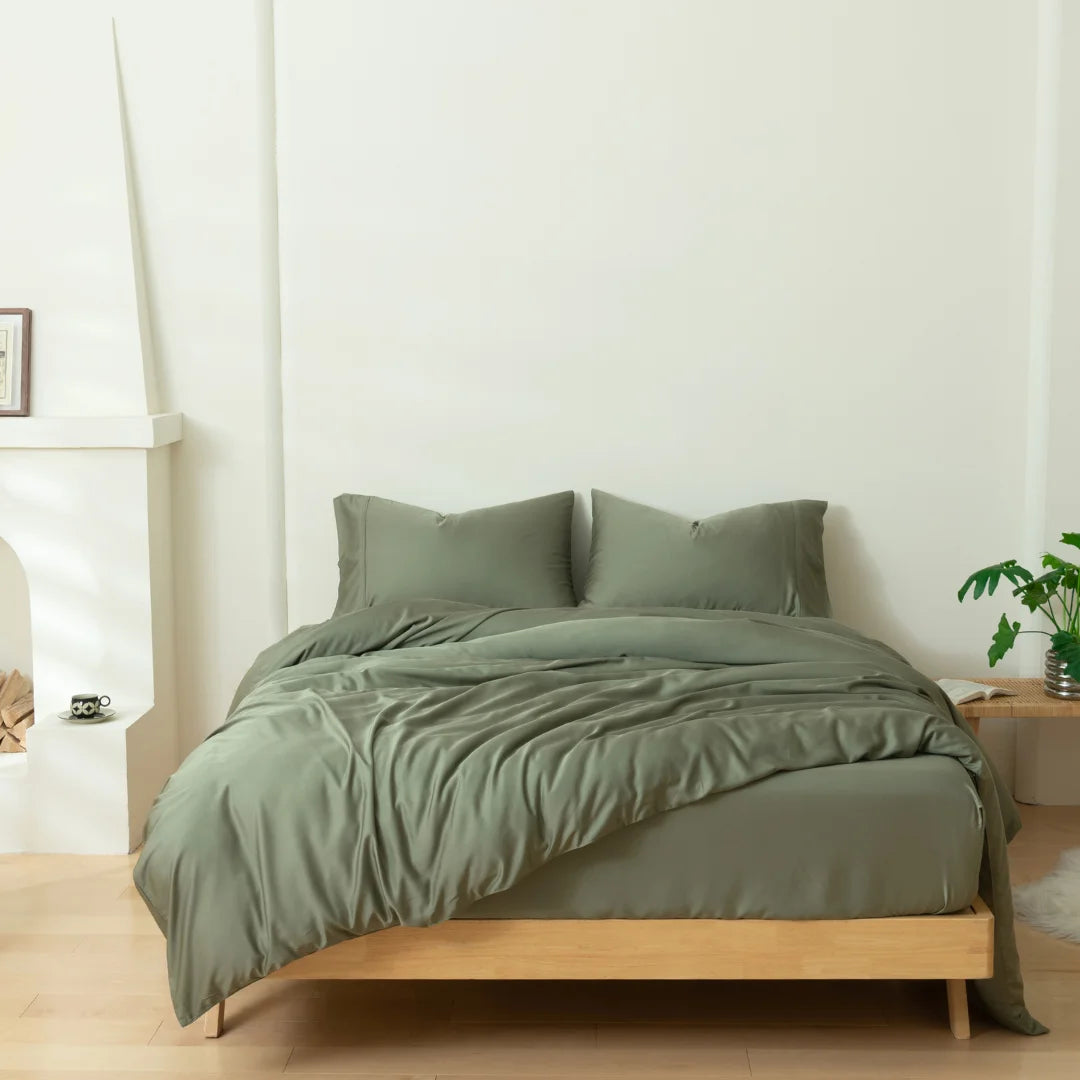 A neatly made bed with an environmentally friendly Linenly Moss Bamboo Quilt Cover in a serene, minimalist bedroom with a wooden bed frame, a small plant, and a decorative fireplace.