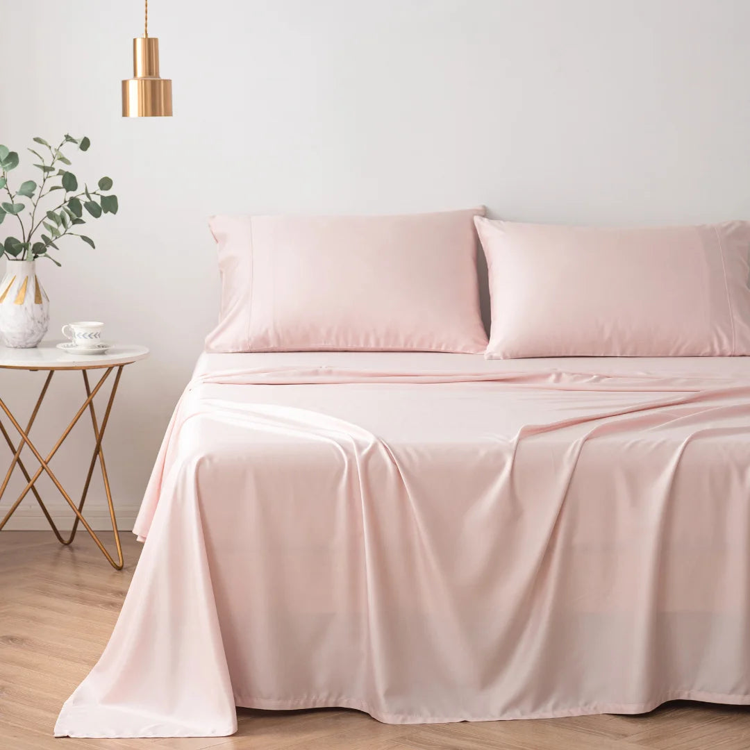 A serene and elegant bedroom featuring a neatly made bed with Linenly's ultra-soft Bamboo Sheet Set in Blush, complemented by a small gold side table with decorative items and a modern hanging pendant light.