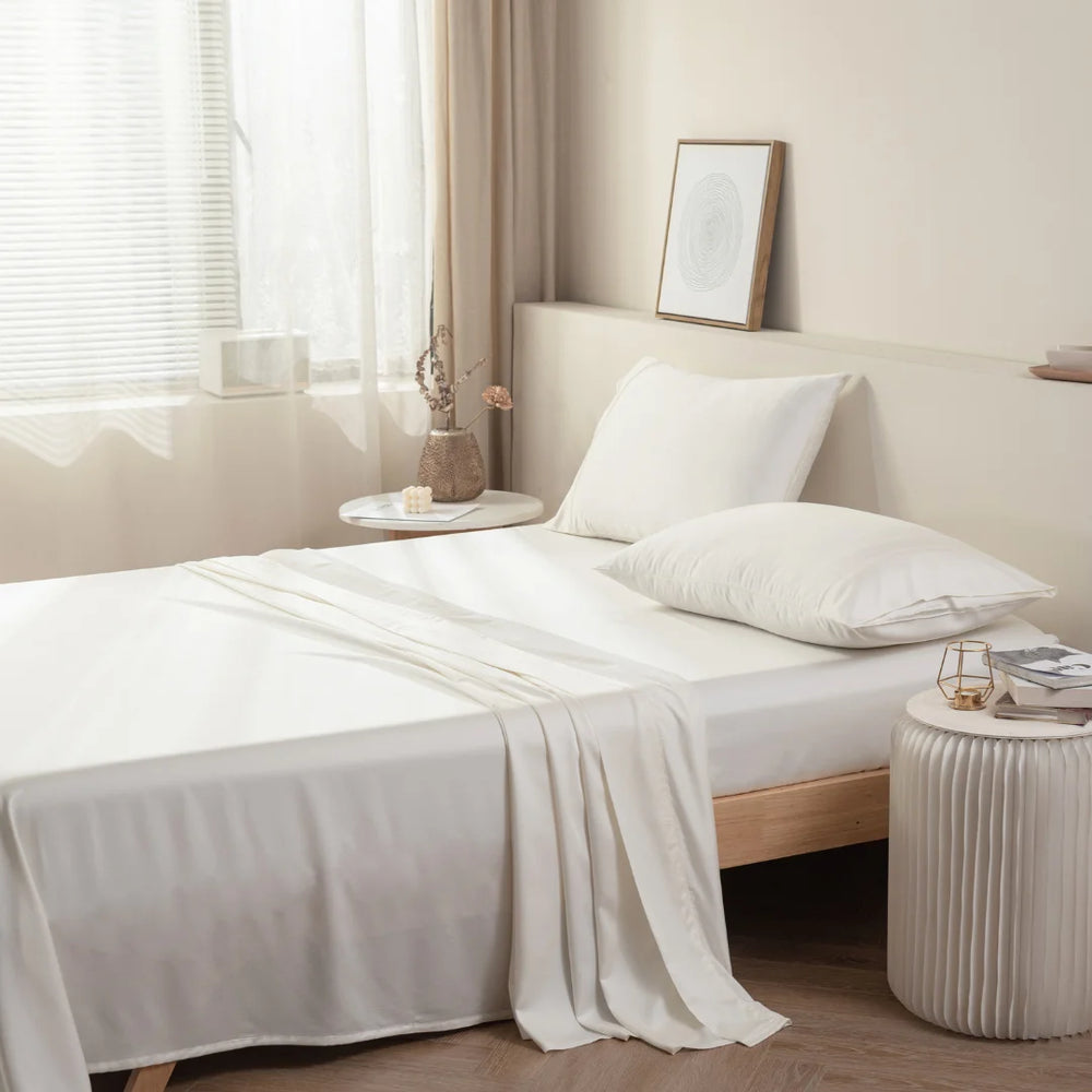 A neatly made bed with Linenly's Ivory Bamboo Sheet Set in a serene and minimalist bedroom, accompanied by soft natural light filtering through a sheer curtain.