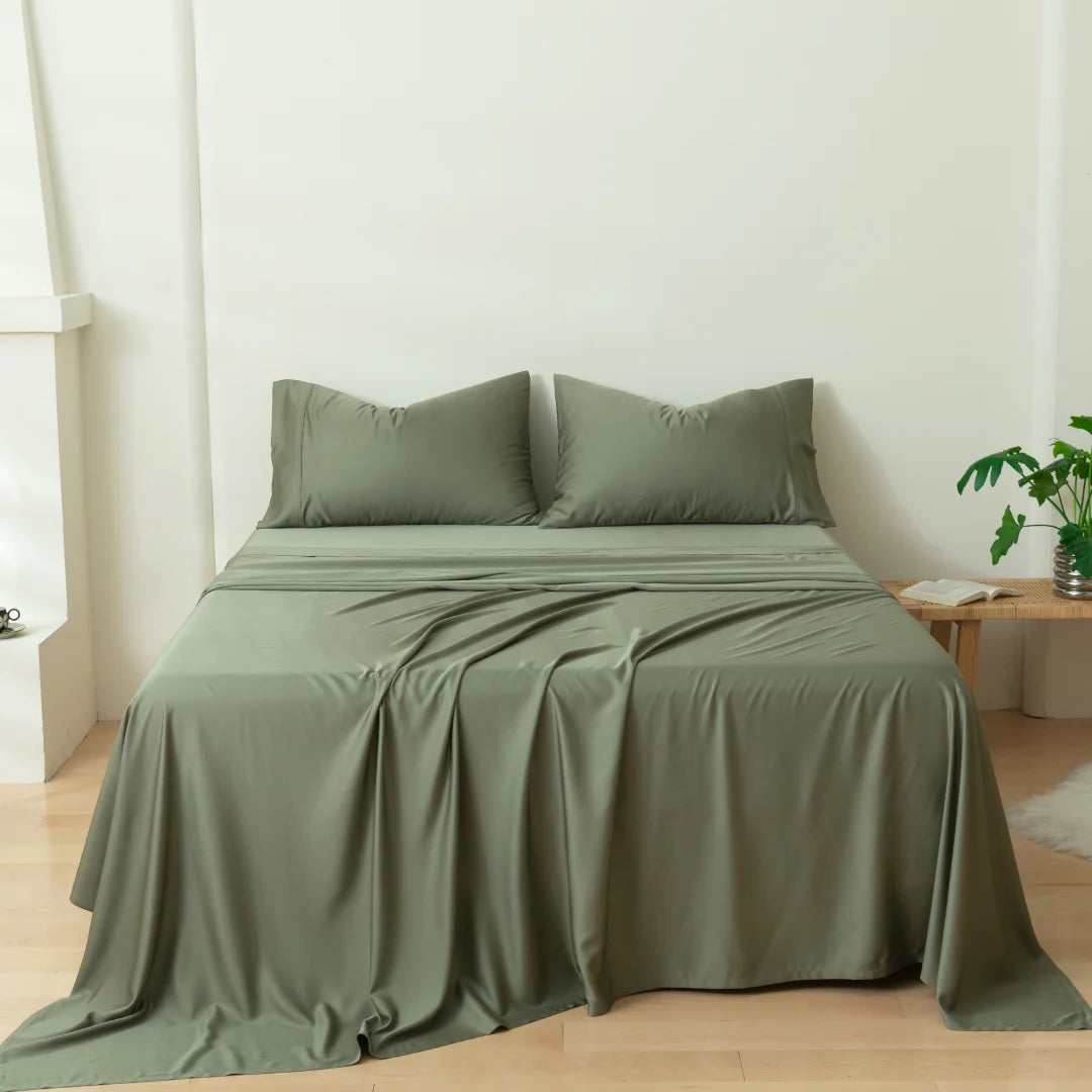 An inviting bedroom with a neatly made bed adorned with Linenly's environmentally friendly Moss Bamboo Sheet Set bedding and pillows, accompanied by a touch of greenery from a potted plant beside it, exuding a serene.