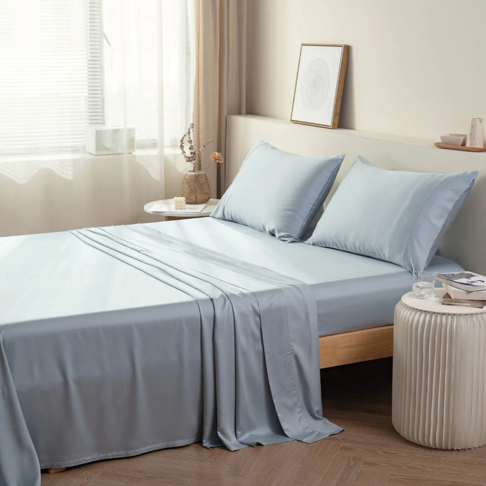 A neatly made bed with a Linenly light blue, breathable bamboo sheet set in a serene and minimalist bedroom setting.