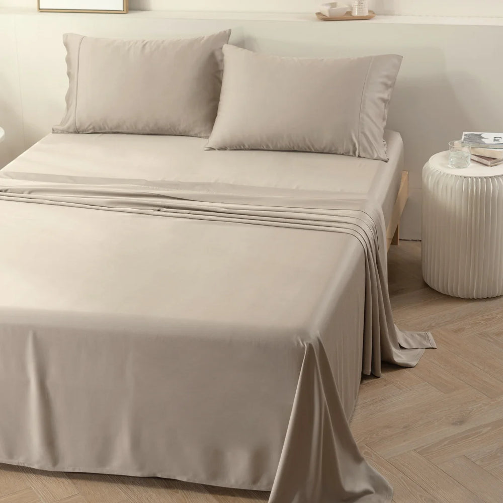 A neatly made bed with a Linenly taupe-colored bamboo sheet set in a serene and tidy bedroom setting, highlighting eco-conscious living.