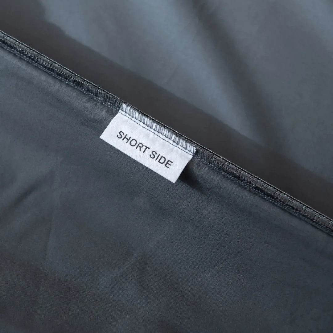 A close-up view of a Linenly Luxe Sateen Fitted Sheet - Charcoal label sewn on the inside of a charcoal fitted sheet with the words "short side" indicating the orientation of the item.