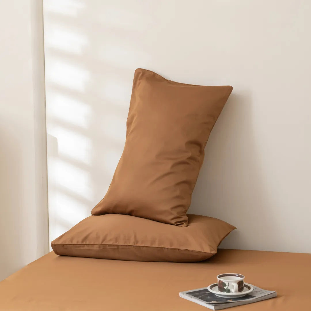 A cozy nook with a brown cushion on a bench, accompanied by a cup of coffee and a book, bathed in soft natural light. The setting is enhanced with a Linenly Luxe Sateen Flat Sheet in terracotta.