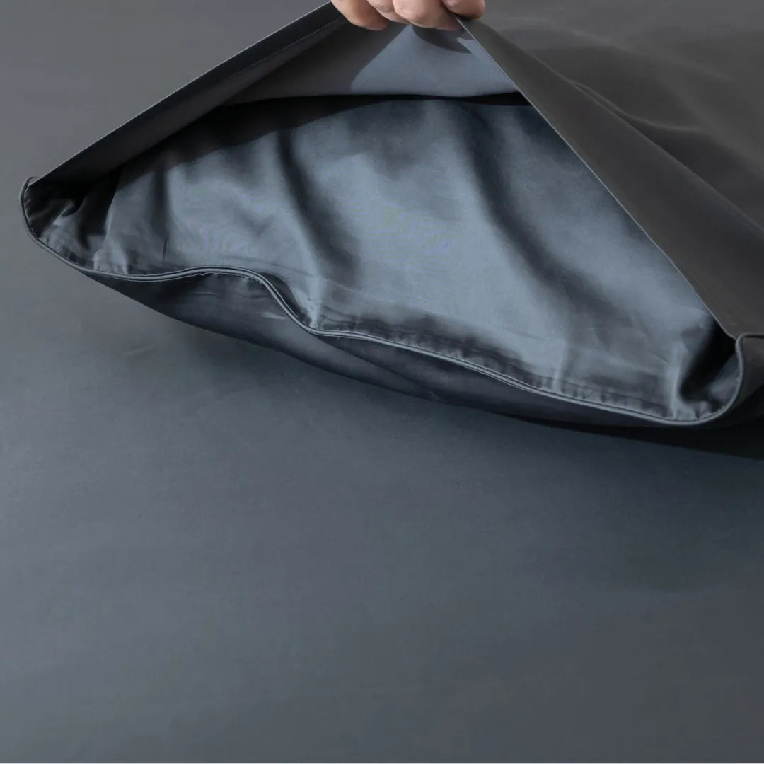 Peeking into the sleek interior of a Linenly Luxe Sateen Pillowcase Set in Charcoal styled modern gray fabric bag against a matching backdrop.