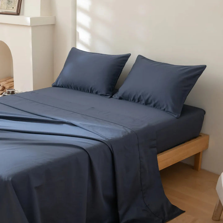 A neatly made bed with smooth, Linenly Luxe Sateen Pillowcase Set - Midnight in a serene bedroom setting.