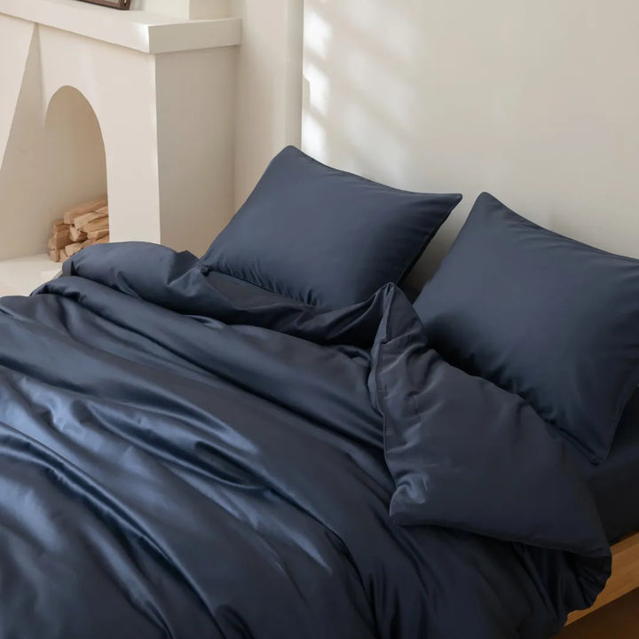 A neatly made bed with Linenly's Luxe Sateen Quilt Cover in Midnight in a room with soft natural light.
