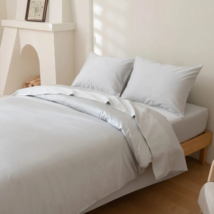 A neatly made bed with Linenly's Luxe Sateen Quilt Cover - Silver in a bright and minimalist bedroom.