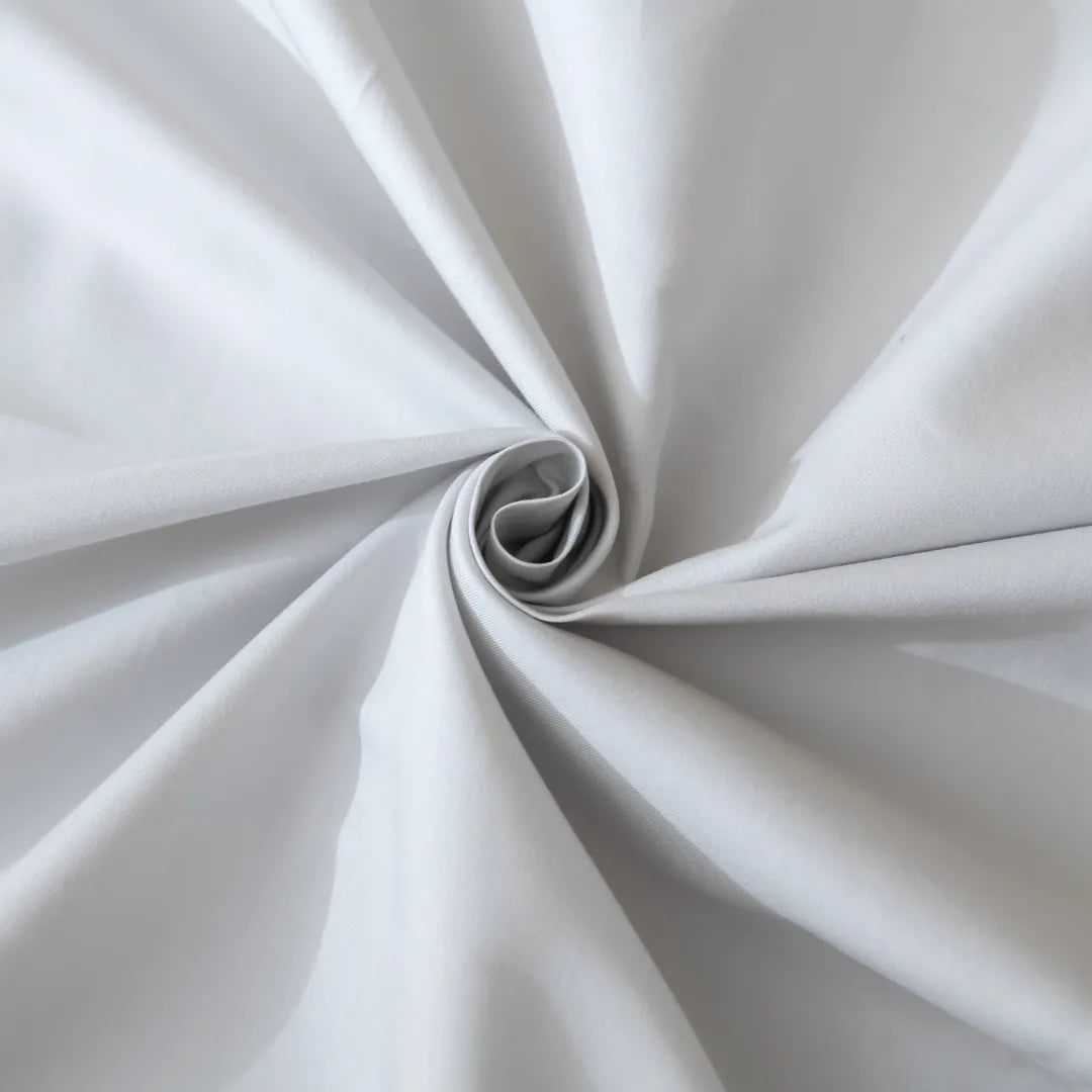 An elegant swirl of Linenly's Luxe Sateen Quilt Cover in Silver creates a mesmerizing spiral pattern, showcasing the subtle play of light and shadow on its textured surface.