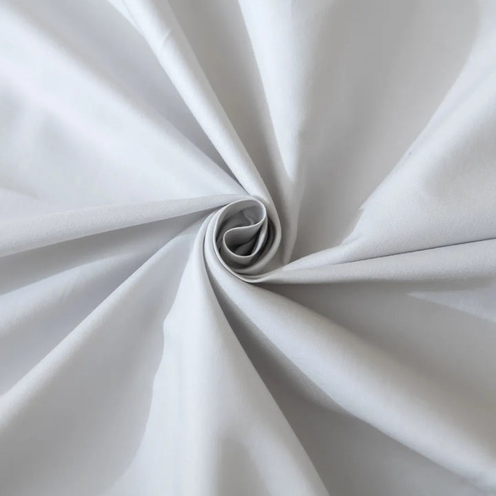 An elegant swirl of Linenly's Luxe Sateen Quilt Cover in Silver creates a mesmerizing spiral pattern, showcasing the subtle play of light and shadow on its textured surface.