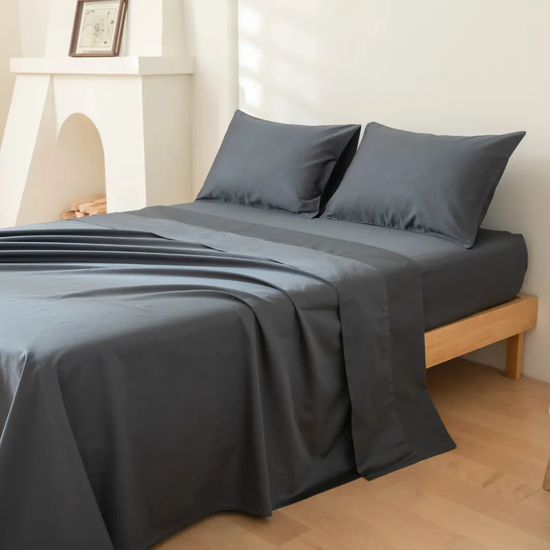 A neatly made bed with Linenly's Luxe Sateen Sheet Set in Charcoal in a clean, minimalist room.