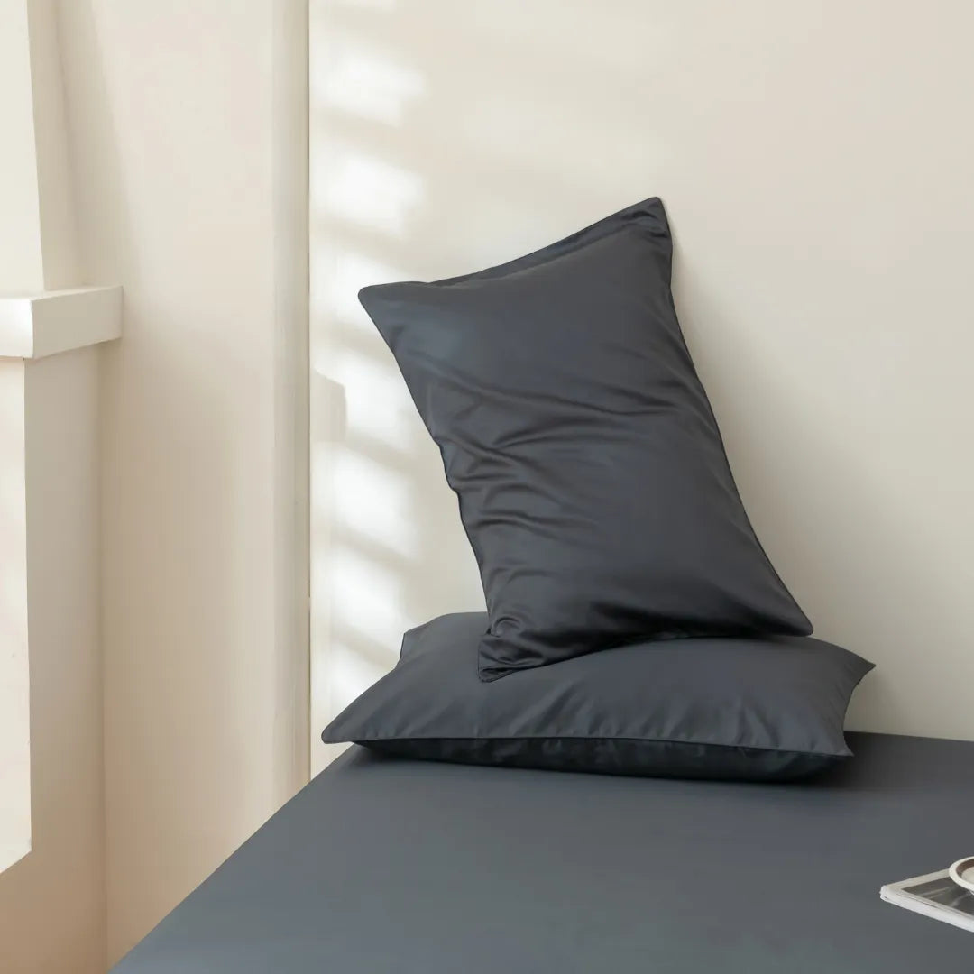 Minimalist modern interior with an elegant dark pillow set on a sleek bench, covered in Linenly Luxe Sateen Sheet Set - Charcoal, bathed in soft natural light casting gentle shadows on a neutral.