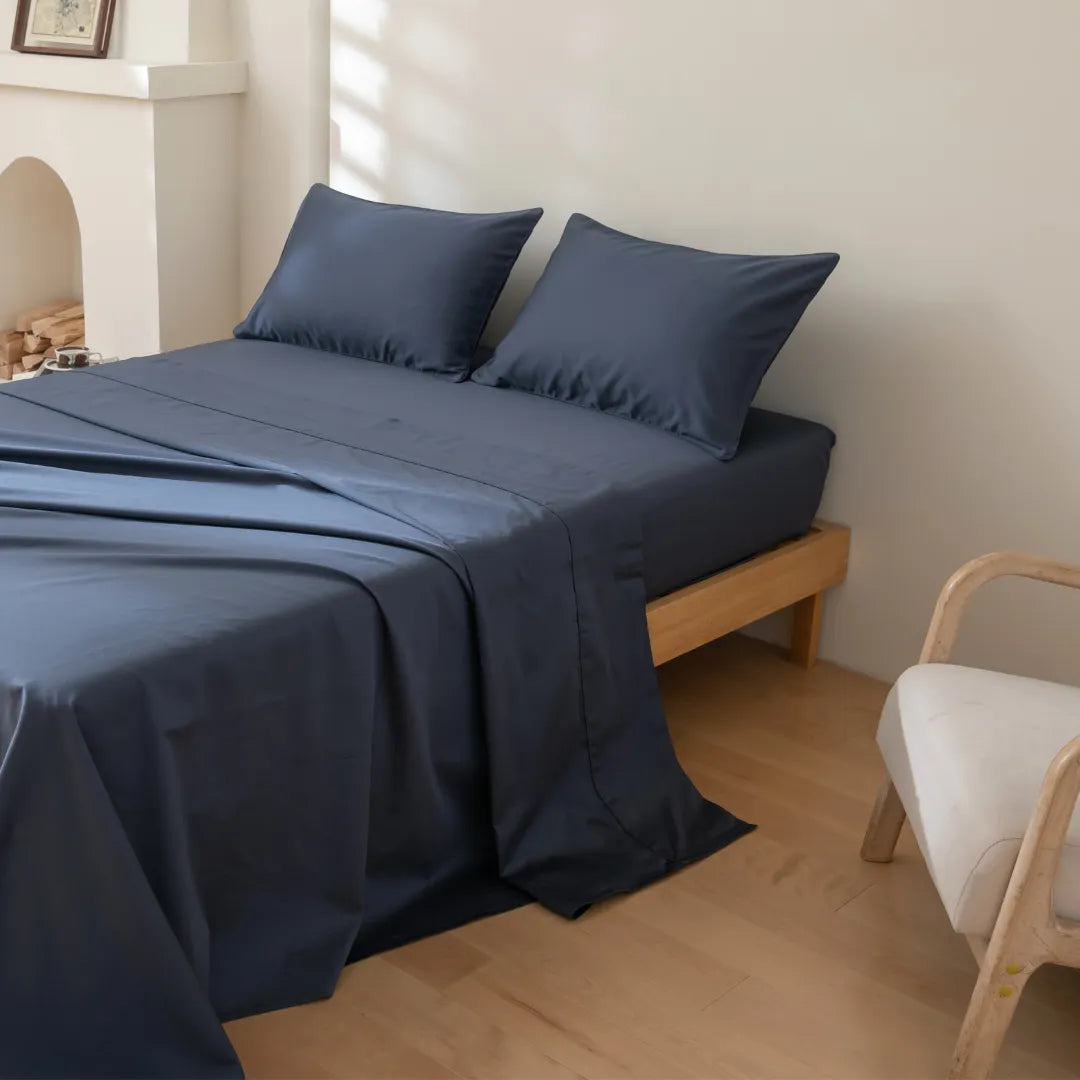 Neatly made bed with Linenly's Luxe Sateen Sheet Set in Midnight Blue in a bright, minimalist bedroom setting.