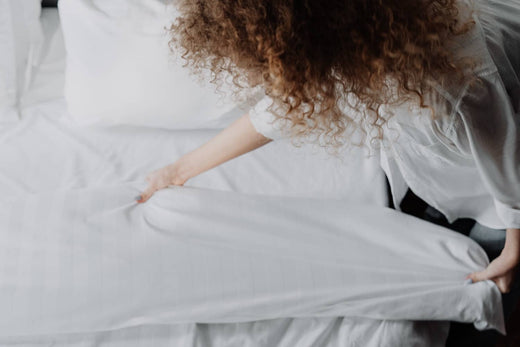 A woman making a bed with white sheets