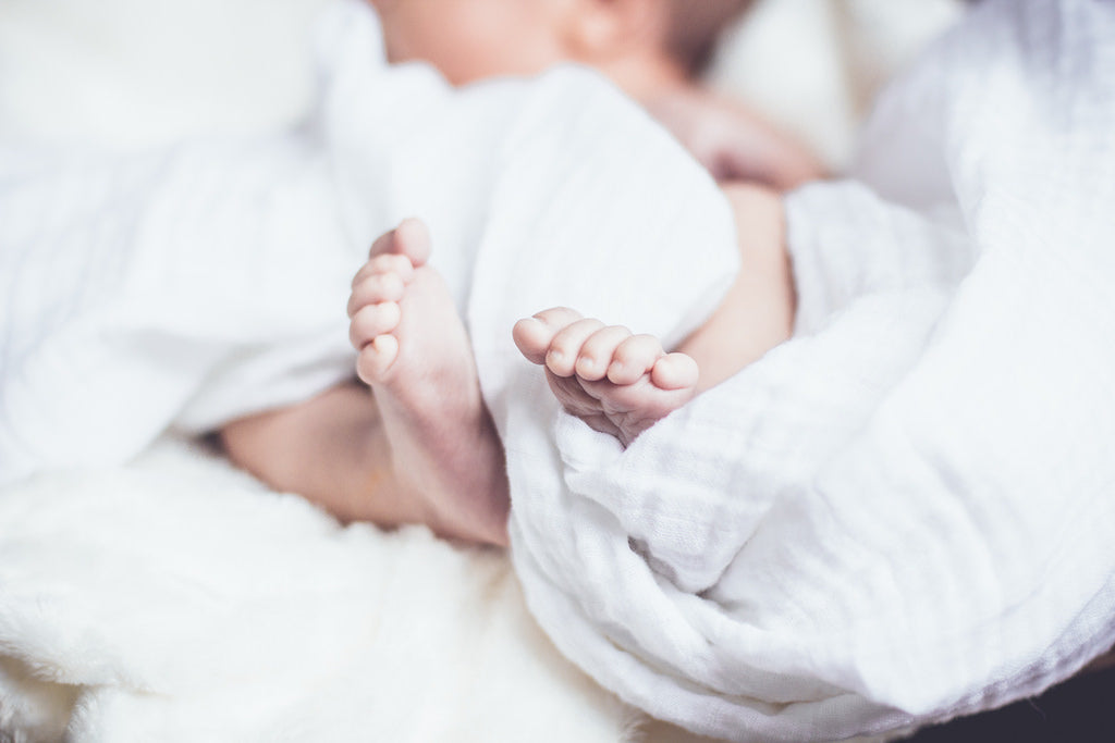 A baby is sleeping on white sheets, and the feet are visible.