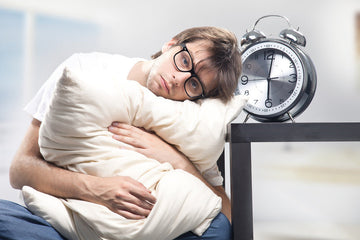 A man hugging a white pillow next to an alarm clock