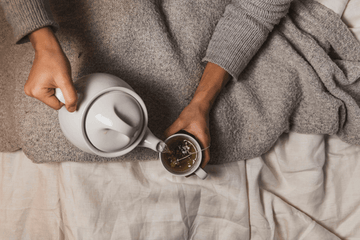 a person pouring tea with a tea pot while in bed