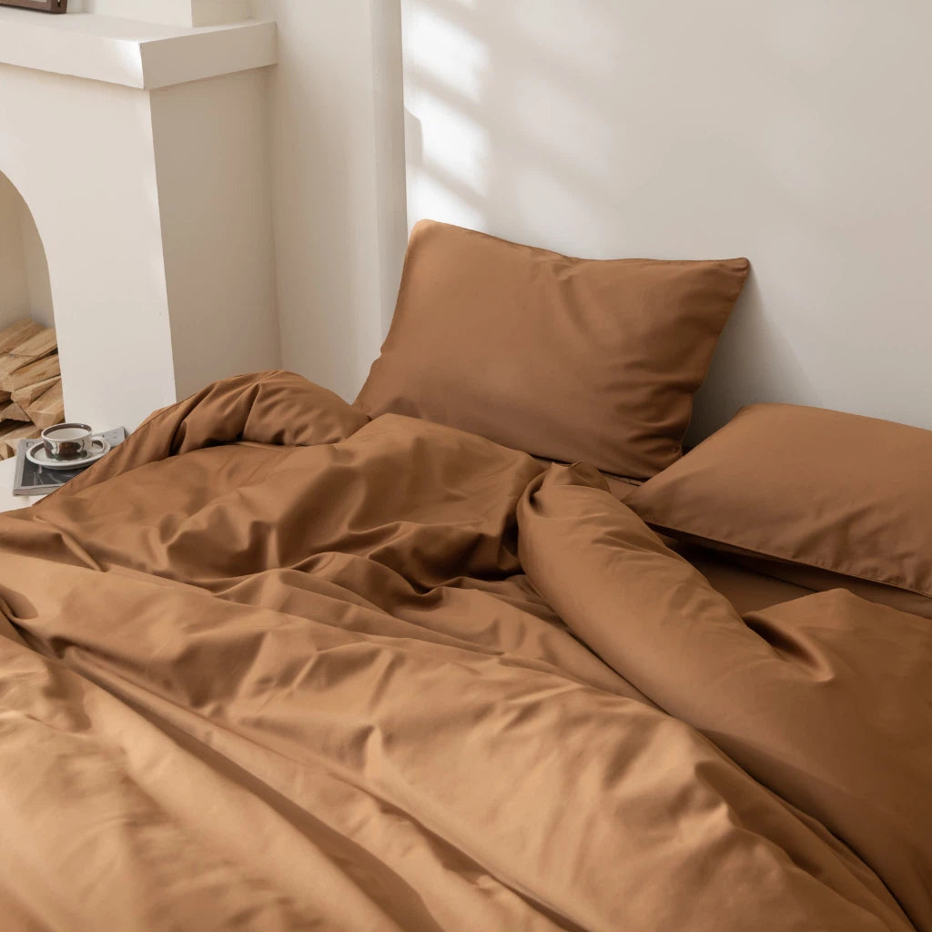 A neatly arranged bed with crumpled caramel-colored linens in a room with soft natural lighting.