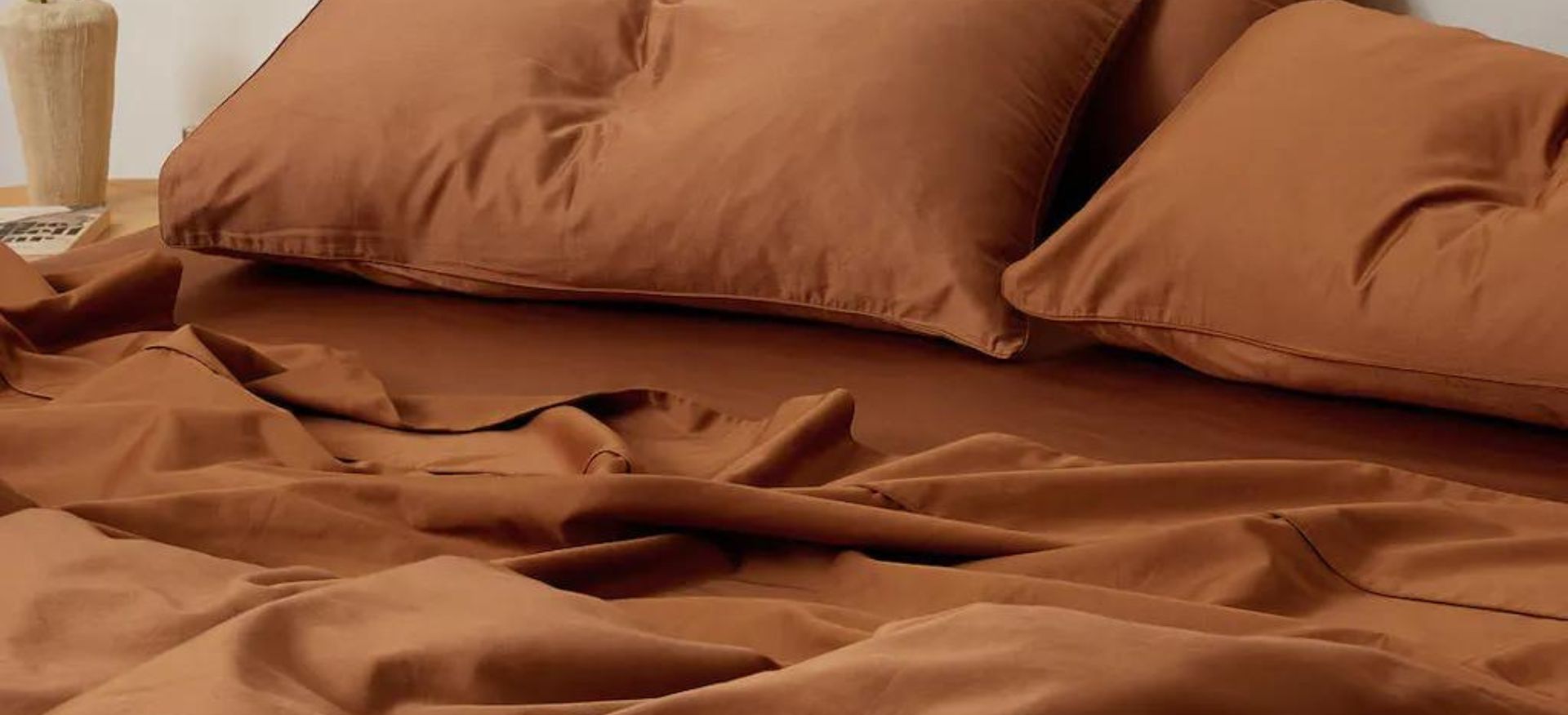 A cozy bedroom scene with rumpled terracotta-colored bed sheets and fluffy pillows inviting relaxation.