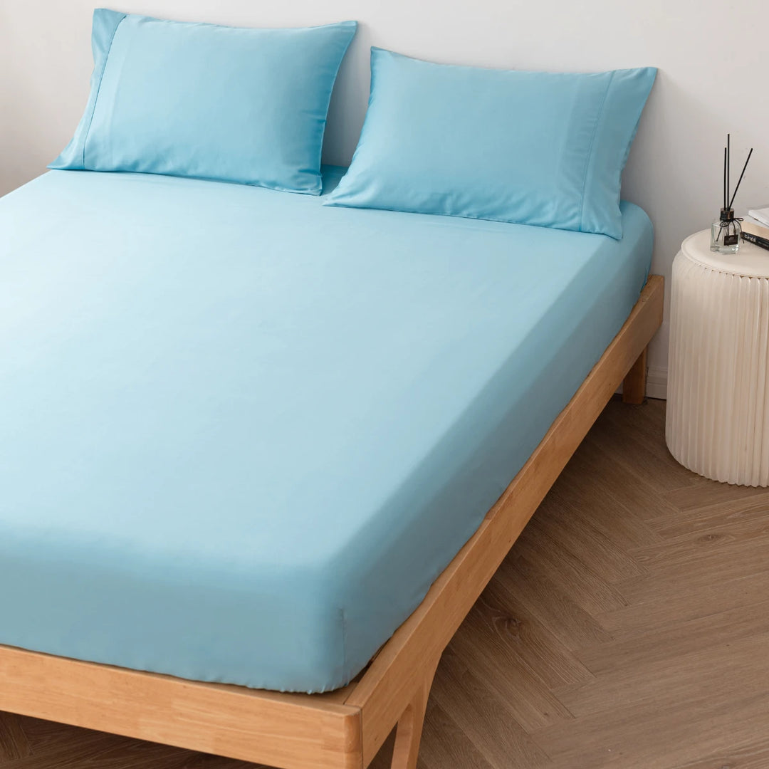 A neatly made bed with Linenly Aqua Blue Bamboo Fitted Sheets on a wooden bed frame, accompanied by a nightstand with a small clock and a white cylindrical container.