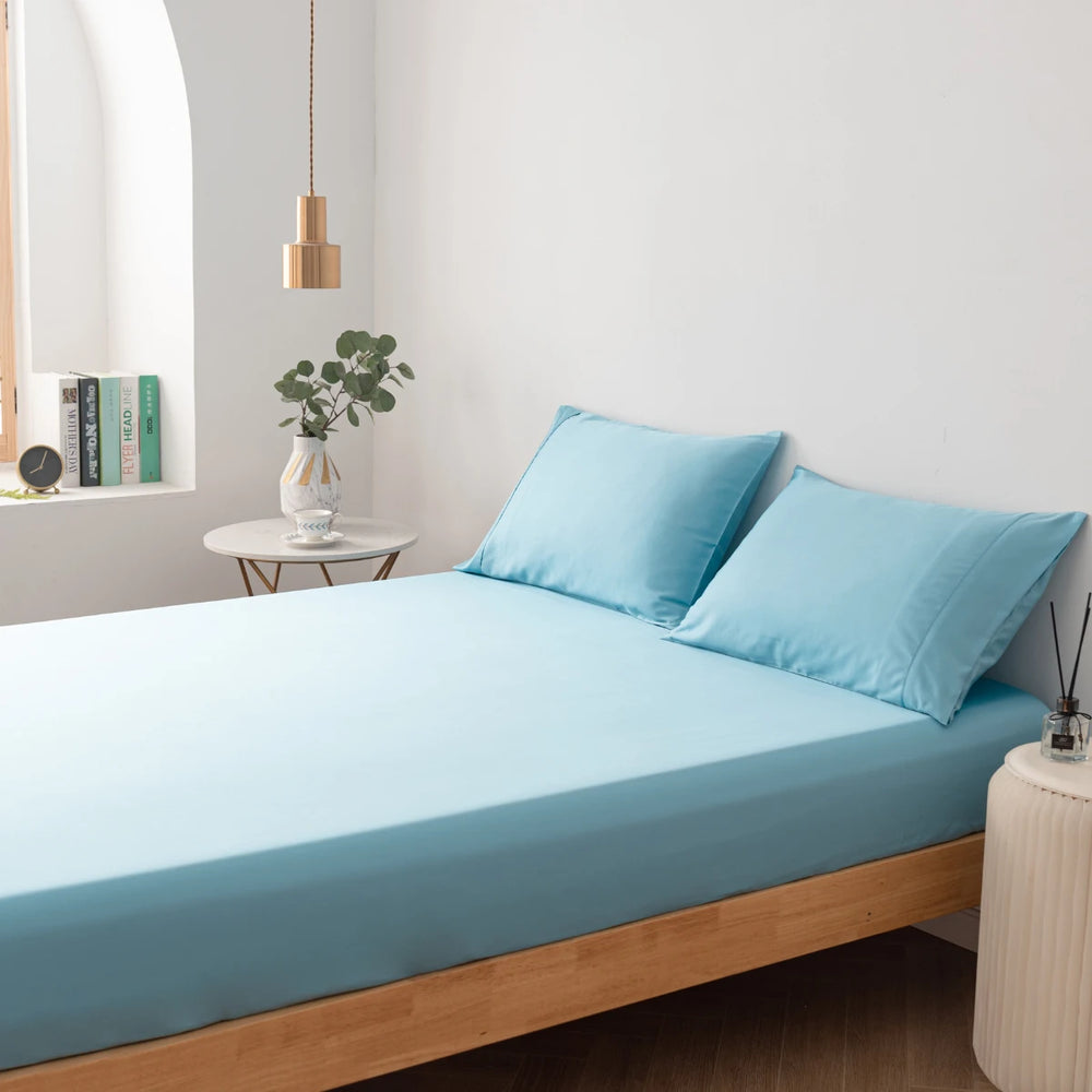 A neatly made bed with Linenly Aqua Blue Bamboo Fitted Sheets in a minimalist style bedroom with soft natural lighting.