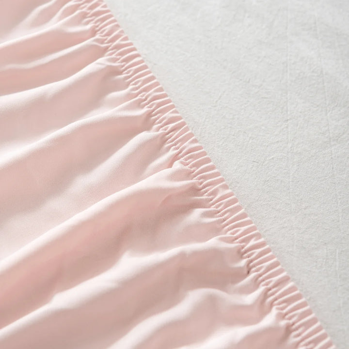 Close-up of Linenly blush bamboo fitted sheets with elastic ruching on the edge, against a neutral textured background.