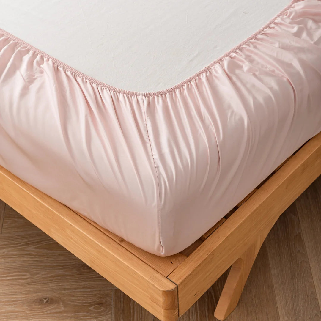 A Linenly Bamboo Fitted Sheet in Blush color neatly wrapped around a mattress on a wooden bed frame.