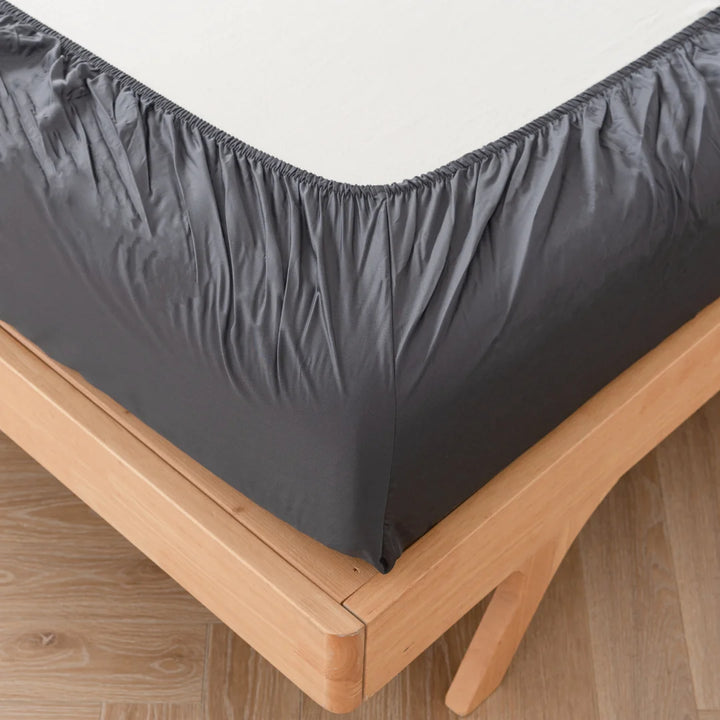 A neatly fitted Linenly Bamboo Fitted Sheet in Charcoal on a wooden bed frame, emphasizing the corner detail where the sheet tucks under the mattress.