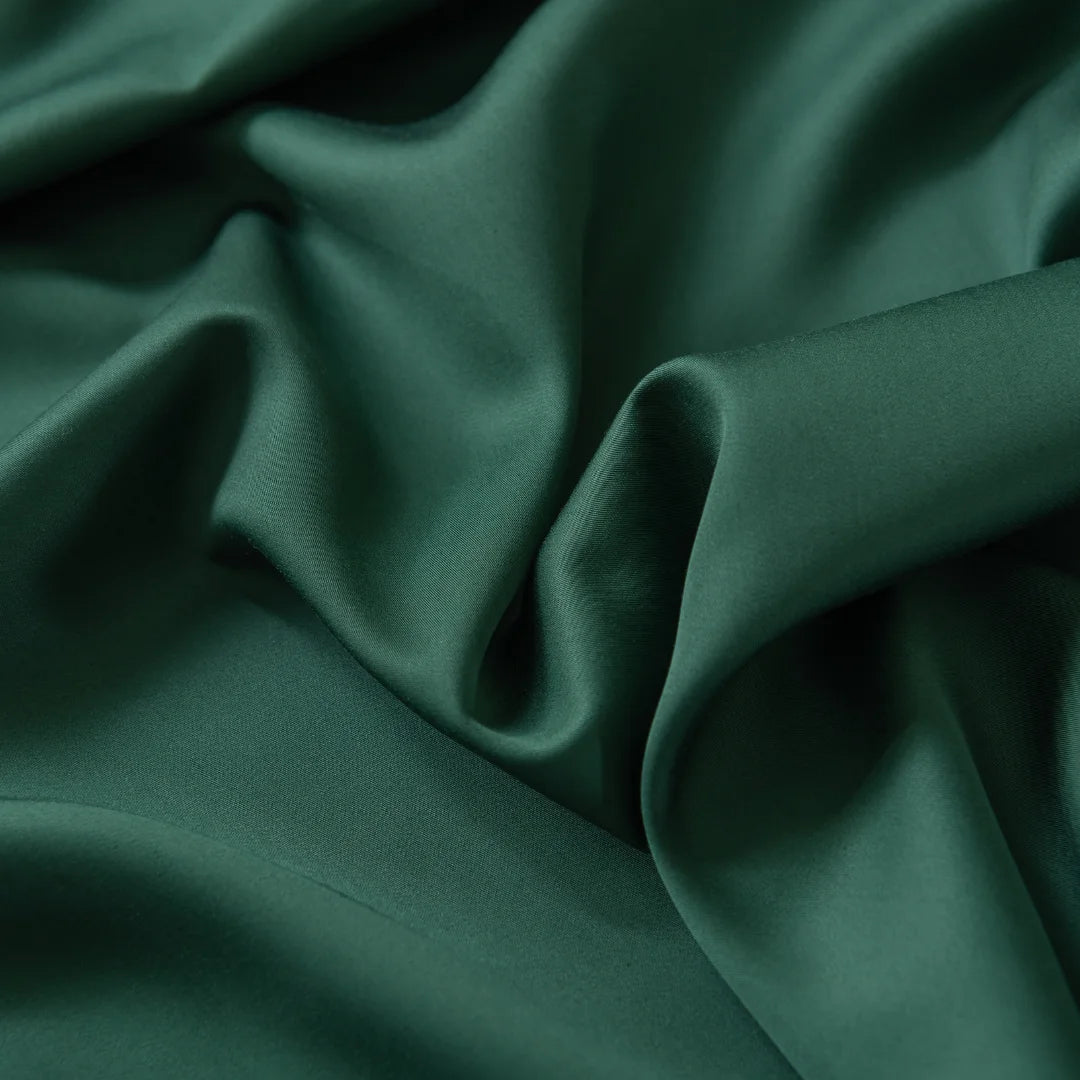 A close-up of the Bamboo Fitted Sheet - Evergreen by Linenly shows its emerald green fabric with smooth folds and a slight sheen, highlighting its luxurious texture and soft drape.