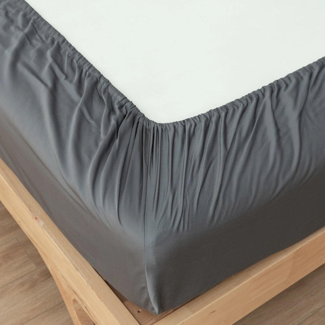 A neatly made bed with a Linenly Granite Grey Bamboo Fitted Sheet on the mattress, offering sumptuous softness.