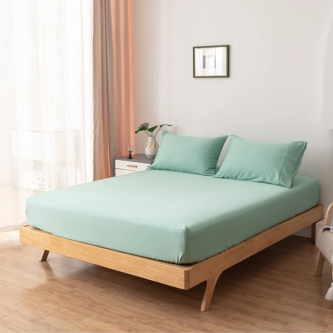 A neatly made bed with a wooden frame and Linenly's Bamboo Fitted Sheet in Green Sheen in a bright, minimalist bedroom.
