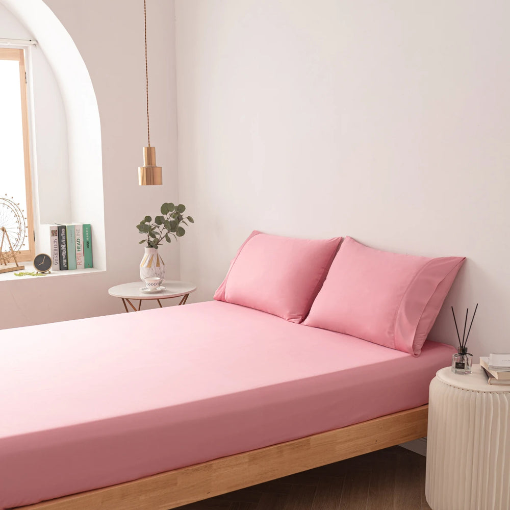 A serene and minimalist bedroom with a comfortable bed dressed in Linenly's Bamboo Fitted Sheet in Light Rose, complemented by a tranquil decor and ambient lighting, providing a peaceful retreat.