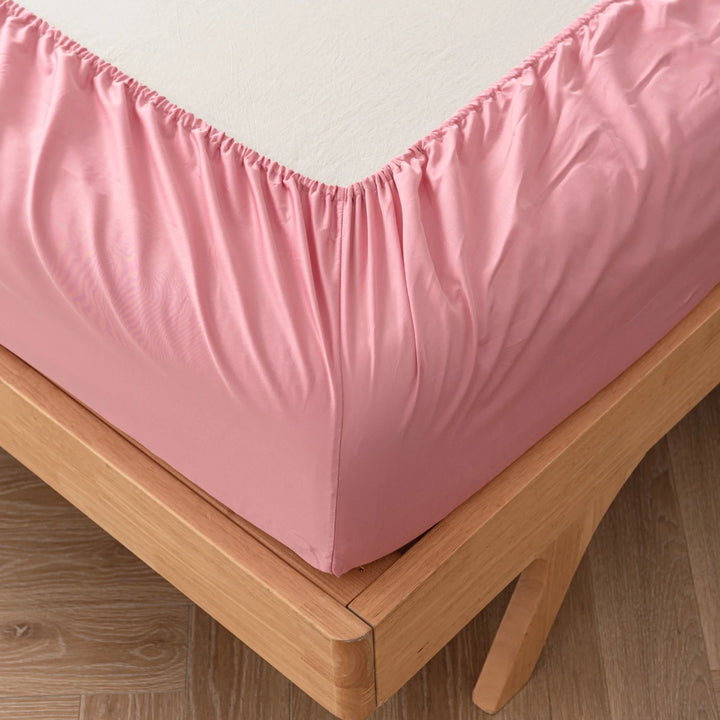 Pastel pink Linenly bamboo fitted sheet neatly covering a mattress on a wooden bed frame, providing a soft and cozy feel to the bedroom decor.