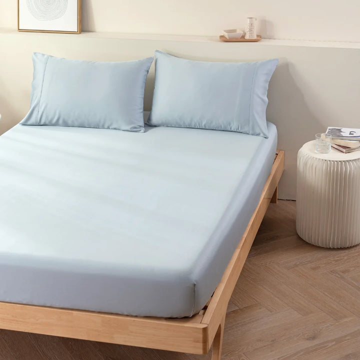 A neatly made bed with Linenly's Bamboo Fitted Sheet in Pale Blue on a simple wooden frame, complemented by a minimalist nightstand and calming wall art in a serene bedroom setting.