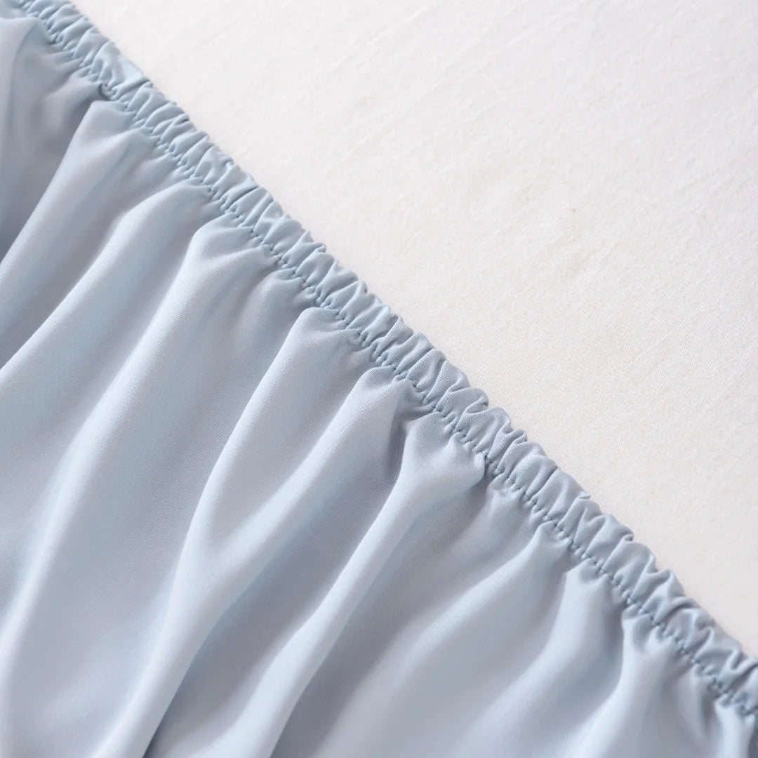 Close-up of a neatly sewn elasticated ruffle on a light grey, sustainable Linenly bamboo fitted sheet in Pale Blue, illustrating detailed textile work and fabric quality.