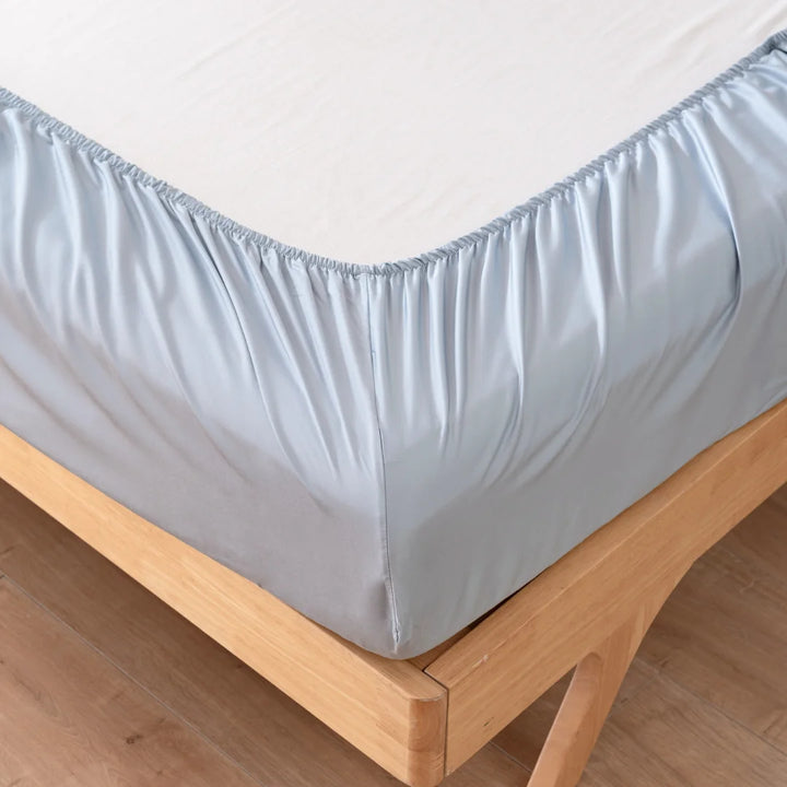 A Linenly bamboo fitted sheet in pale blue neatly covers a mattress on a wooden bed frame, showcasing its snug corners and smooth, cooling touch surface.