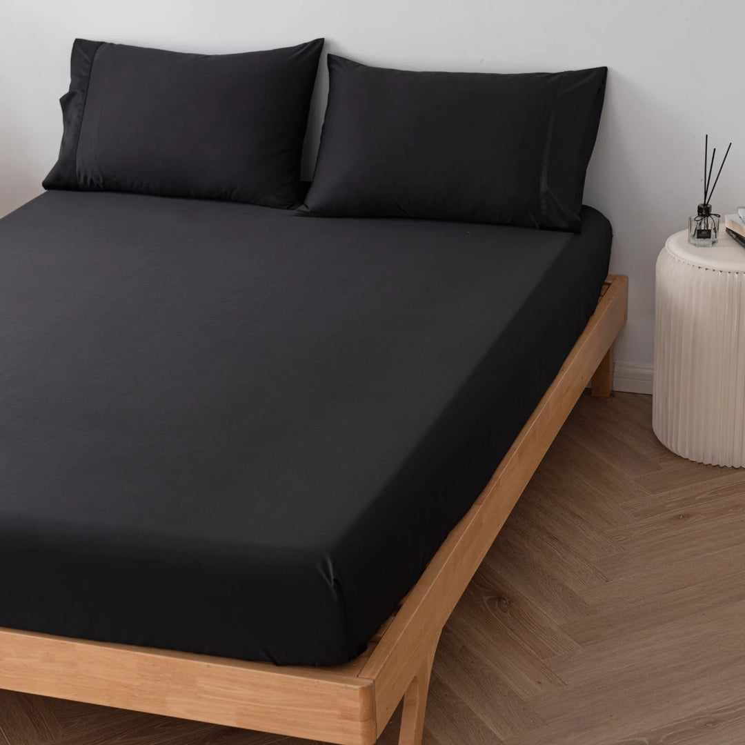 A neatly made bed with a wooden frame and Linenly's Black Bamboo Fitted Sheet in a simple, modern bedroom setting, exuding comfort.