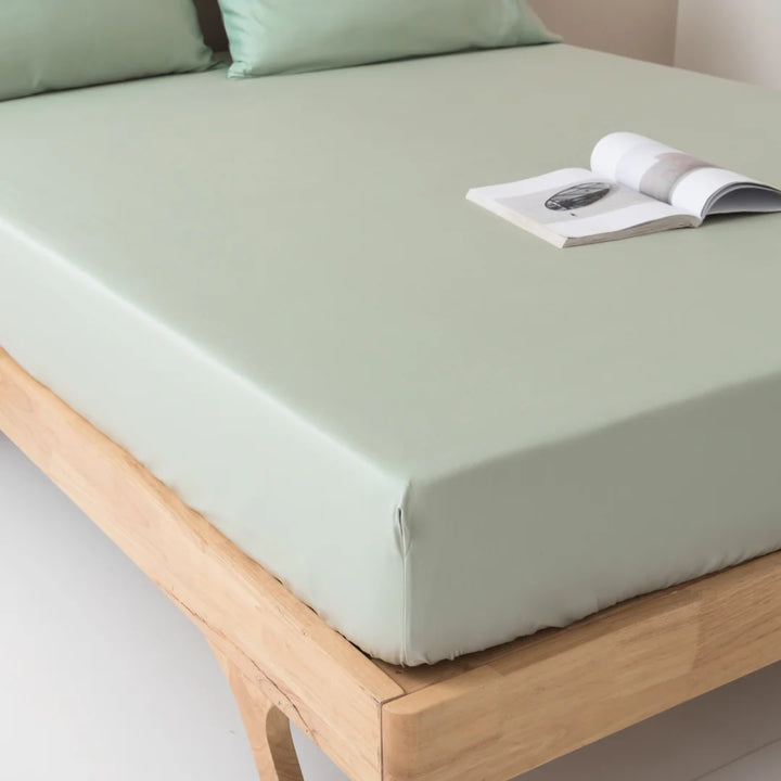 A neatly made bed with smooth Linenly sage bamboo fitted sheets and an open magazine resting on it, invoking a sense of tranquility and minimalism.