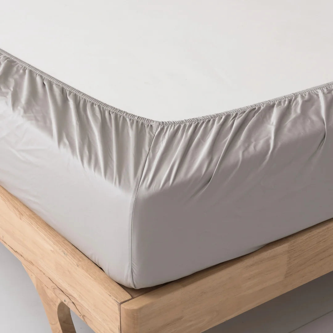 A snugly fitted, Linenly silver-gray bamboo fitted sheet on a wooden bed frame, showcasing its elastic edges for a secure fit, made of breathable bamboo fabric.