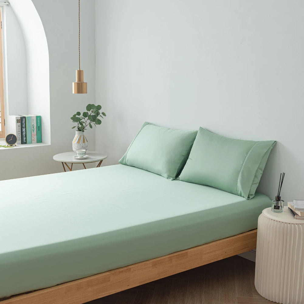 A serene and minimalist bedroom with a neatly made bed featuring Linenly's eco-friendly, summer green bamboo fitted sheets, complemented by a simple side table and soothing wall color, creating a tranquil space for rest.