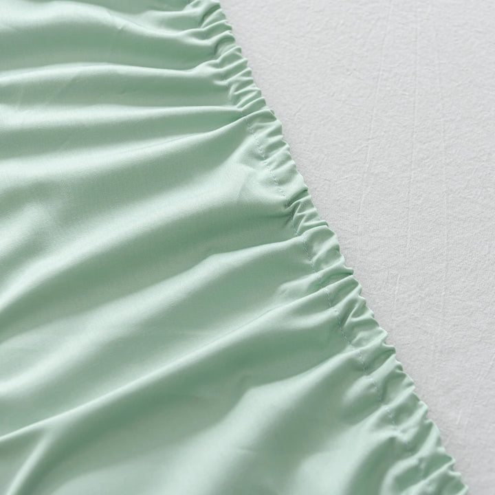 Close-up of Linenly Bamboo Fitted Sheet - Summer Green with elastic gathers lying on a textured white surface.
