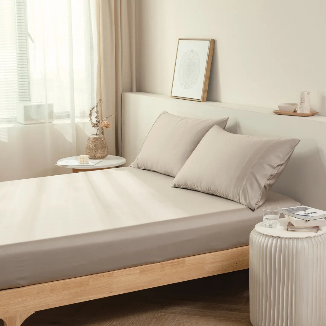 A serene and minimalist bedroom with a neatly made bed, Linenly's bamboo fitted sheet in Taupe, earth-toned linens of breathable bamboo fabric, and simple decorative elements creating a tranquil luxury sleep sanctuary.