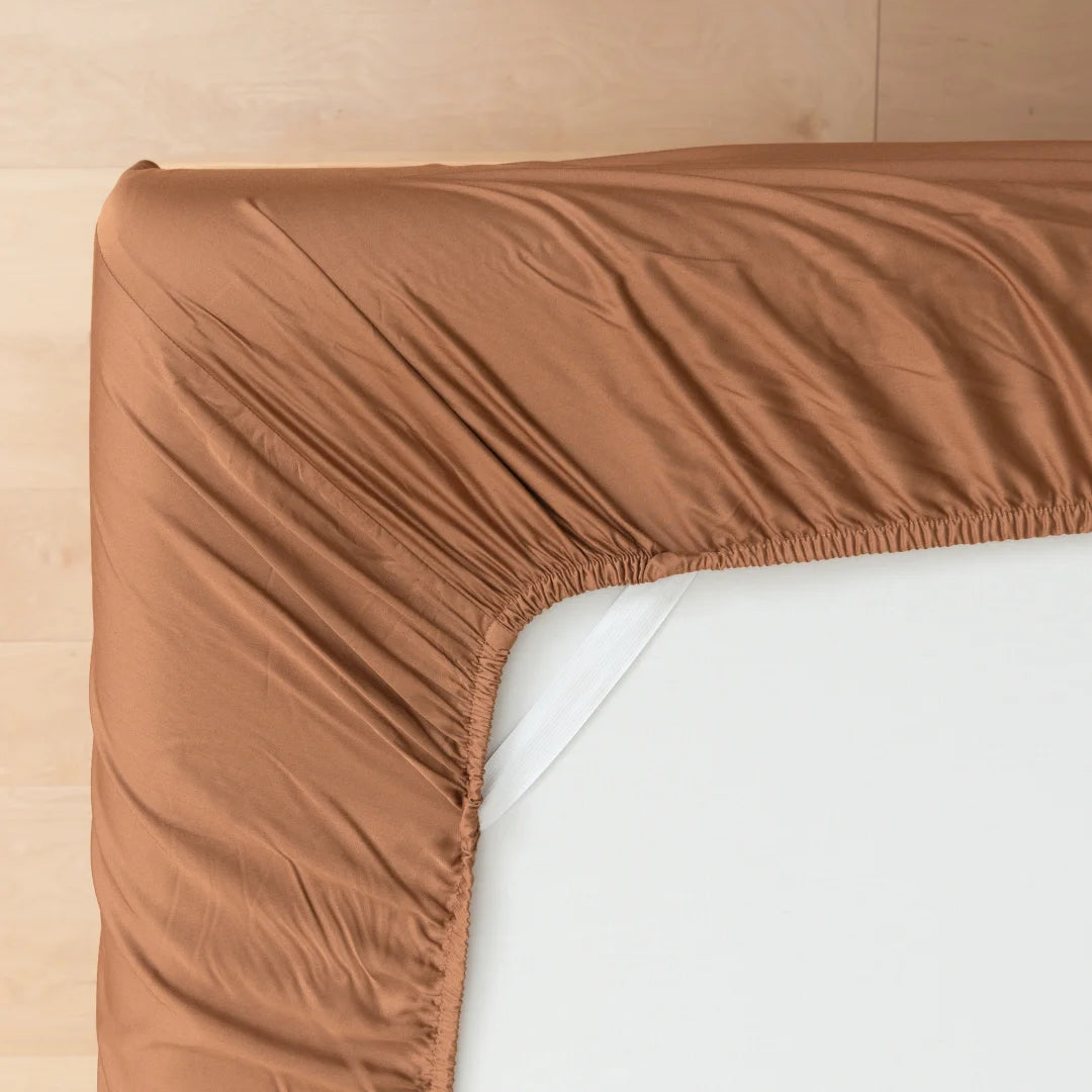 A neatly fitted Linenly Bamboo Fitted Sheet in Terracotta on the corner of a mattress, showcasing a tidy bedroom setting in luxurious comfort.