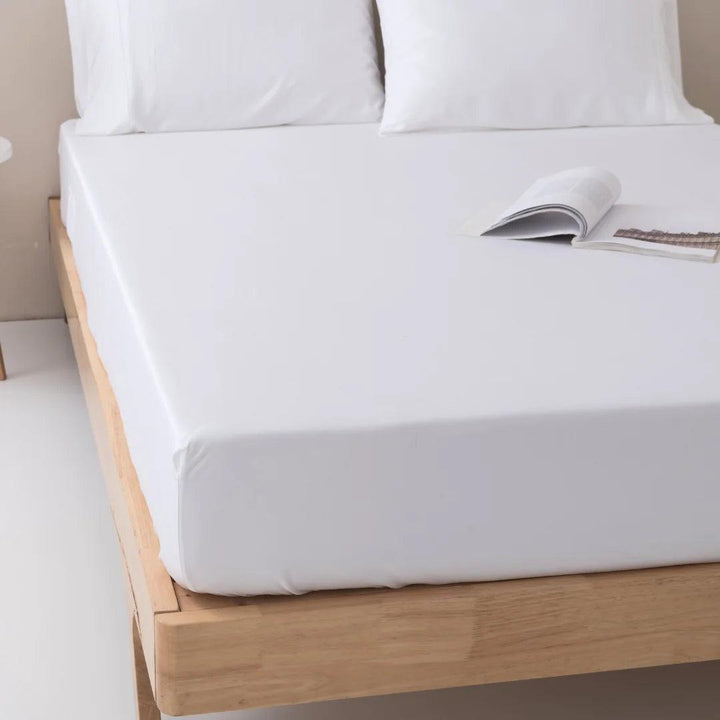 A neatly made bed with crisp white bedding, featuring a Linenly Bamboo Fitted Sheet - White with deep sides, and an open book resting on it, inviting a relaxing reading session.